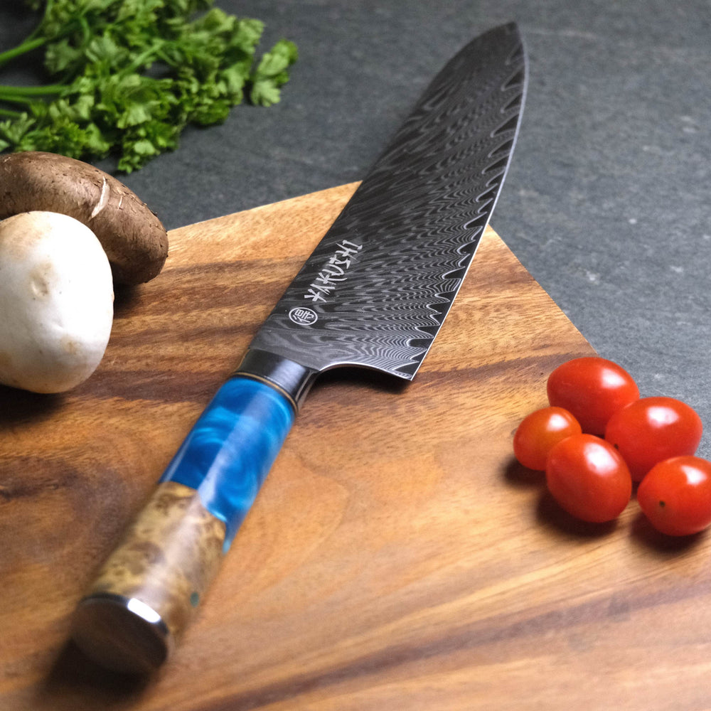 Yakushi Japanese chef knife with blue handle on a wooden cutting board beside mushrooms, herbs and tomatoes
