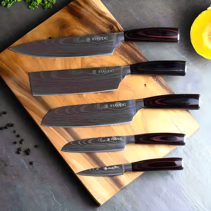 Yakushi 5-piece master chef knife set laid out on a cutting board showing the etched damascus pattern and pakkawood handles.
